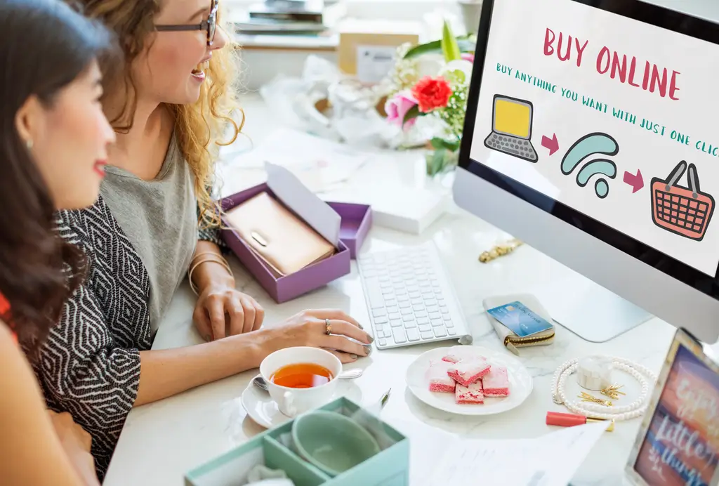 Two women shopping online at a computer, browsing an ecommerce website with a “Buy Online” screen.